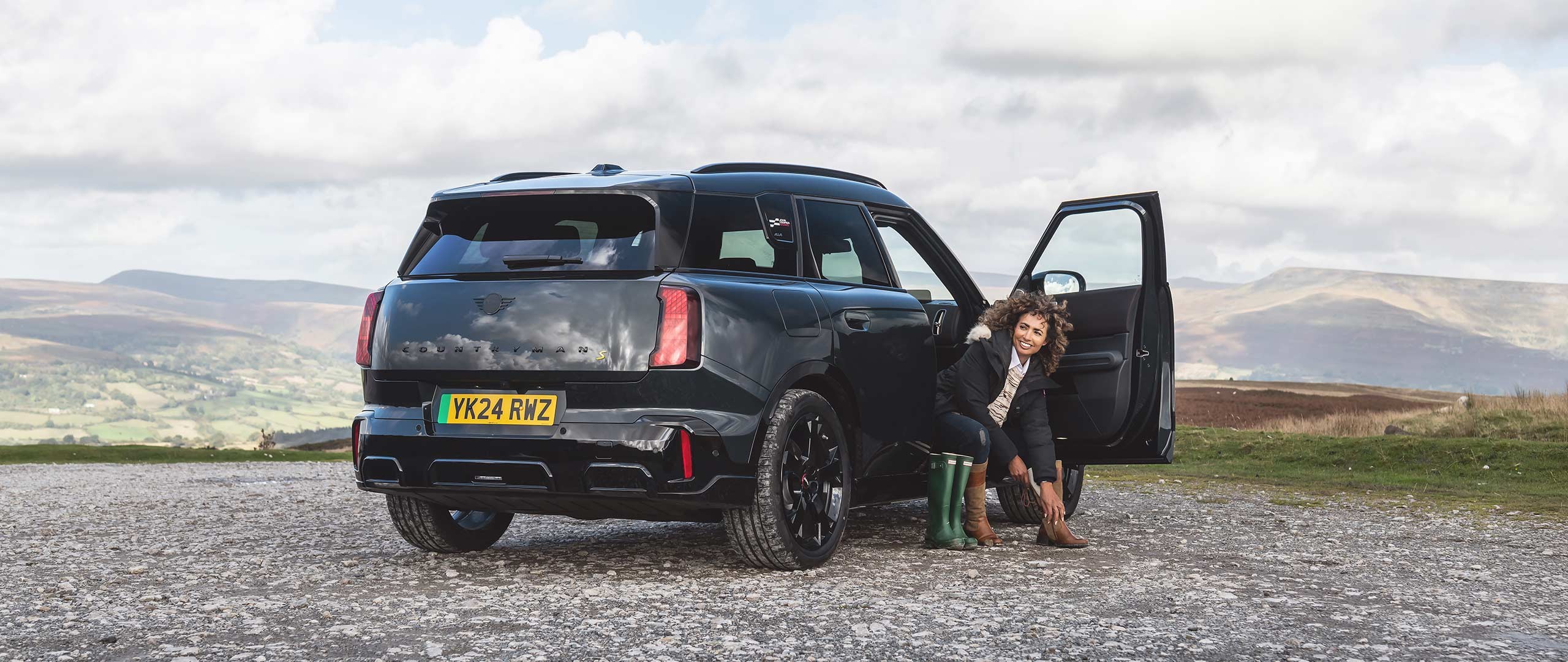 Rear view of the all-electric MINI Countryman in Smokey Green and Vibrant Silver roof parking. 
